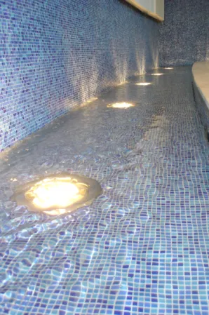 Illuminated underwater lights in a curved pool lined with blue mosaic tiles