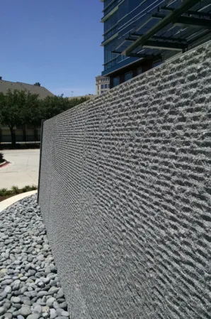 Close-up of a textured granite water wall with cascading water and decorative pebbles
