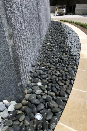 Close-up of a textured granite water wall with cascading water and decorative pebbles