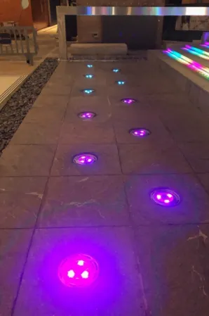Illuminated fountain nozzles glowing purple and blue in a paved walkway
