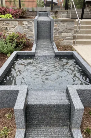 Rectangular granite fountain with cascading water channels and a central basin in a landscaped courtyard