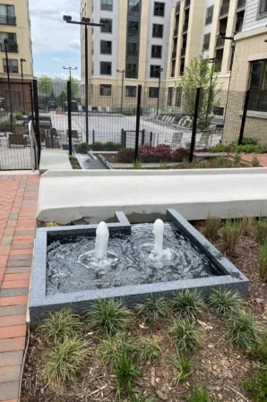 Rectangular granite fountain with two bubbling water jets beneath a stone bench in a landscaped residential courtyard