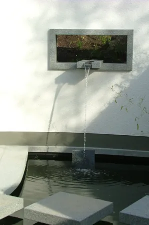 Wall-mounted water spout cascading into a rectangular granite fountain basin