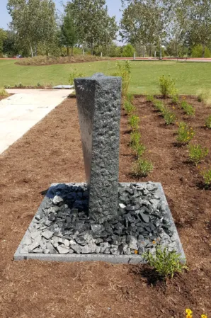 Vertical granite fountain column surrounded by decorative stones in a landscaped garden
