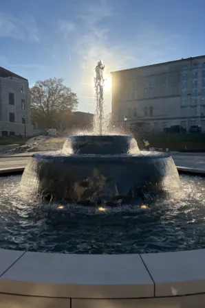 Circular stone fountain with cascading water in front of a historic building