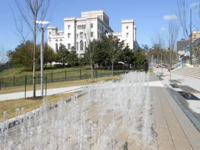 Rows of water jets in a paved fountain plaza with a historic castle-like building in the background