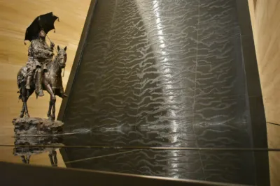 Indoor water wall with a textured flowing surface beside a bronze equestrian sculpture