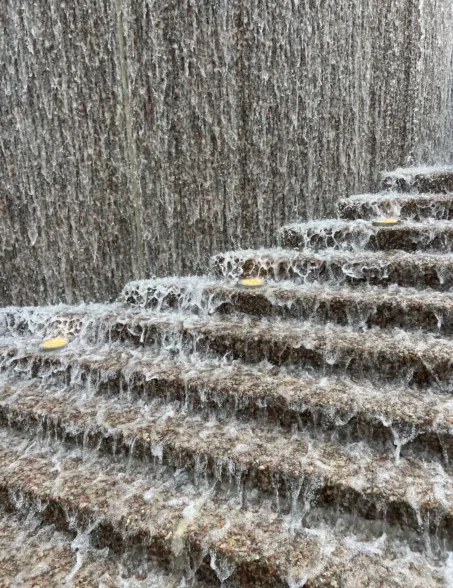 Water cascading down multiple stepped stone ledges, creating a textured waterfall with flowing streams and white foam.