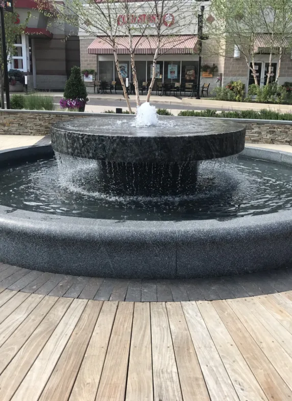 Circular granite fountain with a raised central basin and cascading water in an outdoor shopping plaza
