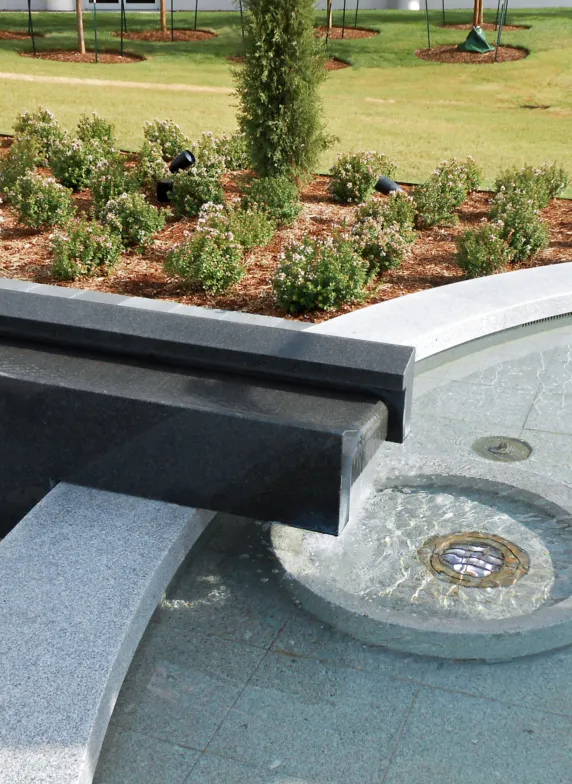 Close-up of a granite fountain with an integrated water channel and circular drain beside a landscaped garden
