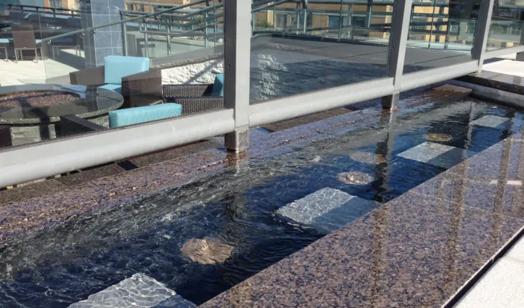 Narrow granite water feature with small fountains and submerged stone blocks in a modern courtyard