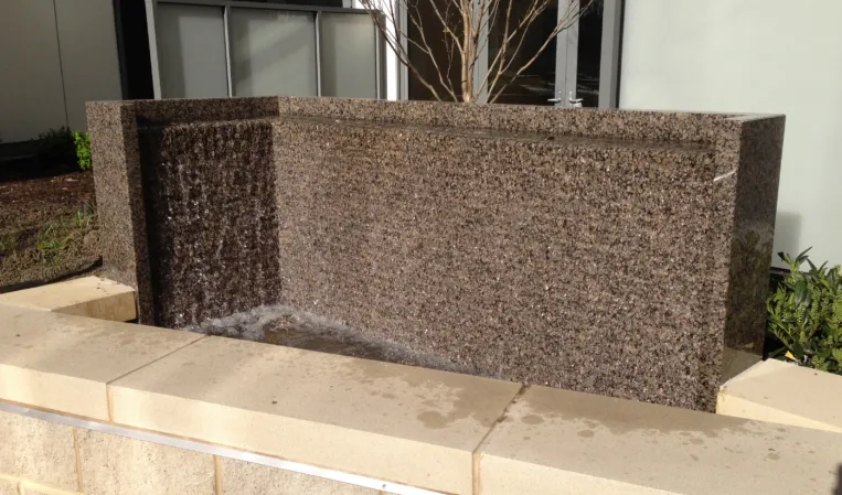 Textured granite water wall with water cascading into a shallow basin