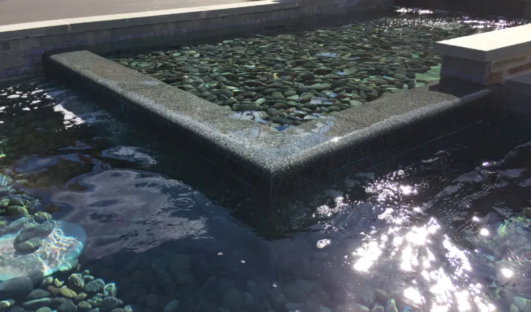 Geometric granite fountain with submerged stone ledges and pebbles beneath clear water