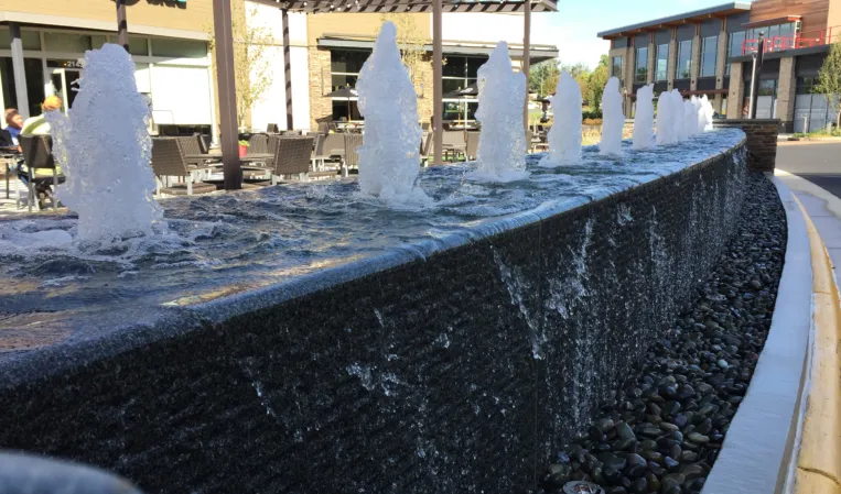 Row of water jets along a curved granite fountain wall with cascading water