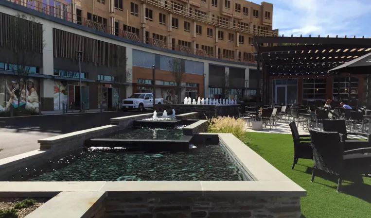 Rectangular stone fountains with water jets beside an outdoor dining area in an urban plaza