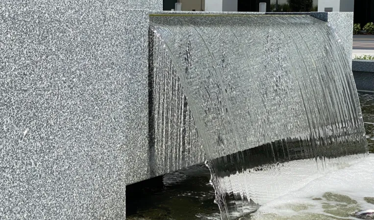 Water cascading over a polished granite wall into a shallow fountain basin