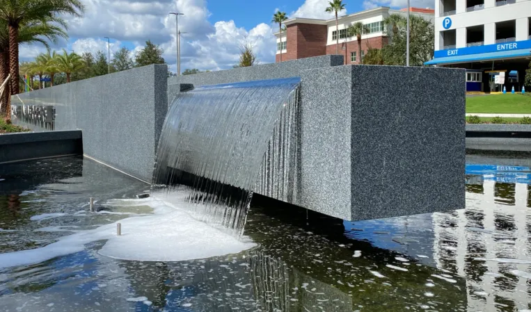 Granite fountain with water cascading over a wide spillway into a reflecting pool