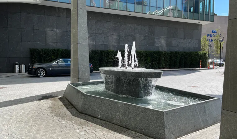 Granite fountain with central water jets cascading into a rectangular basin in an urban plaza