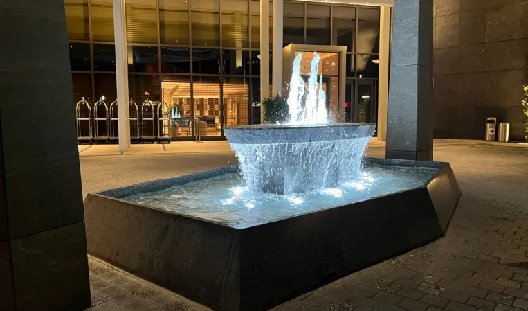 Illuminated granite fountain with cascading water and central jets outside a modern building at night