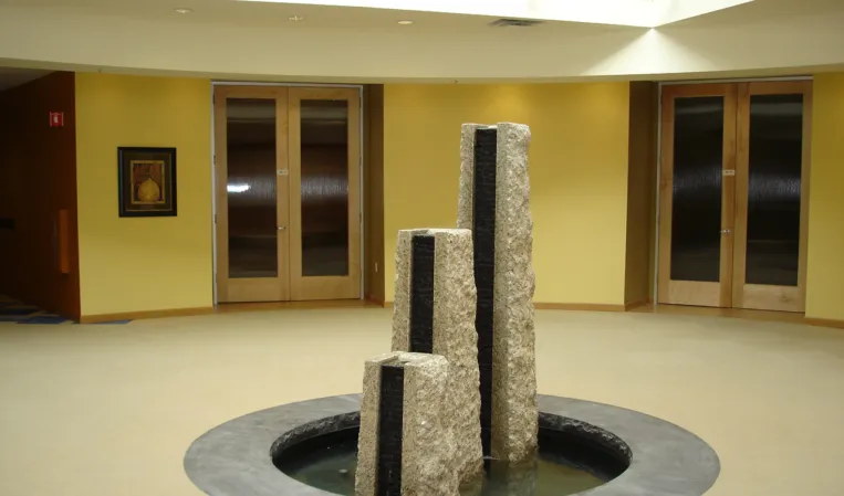 Three vertical rough-hewn granite pillars forming a fountain in a circular indoor basin