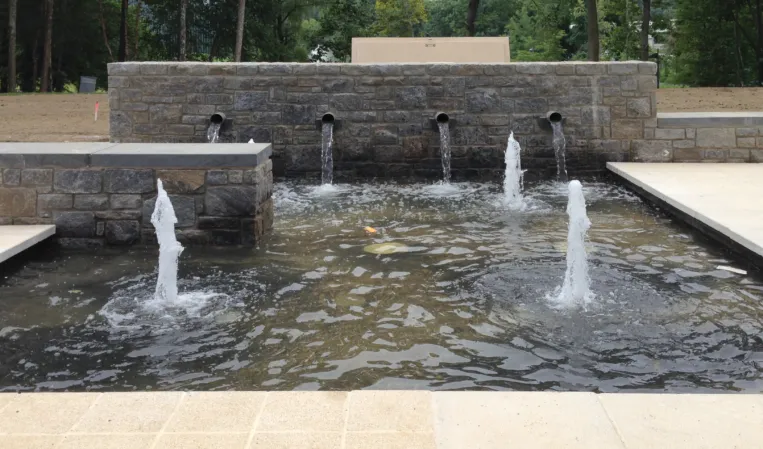 Stone fountain with vertical water jets and spouts flowing from a natural stone wall into a rectangular basin