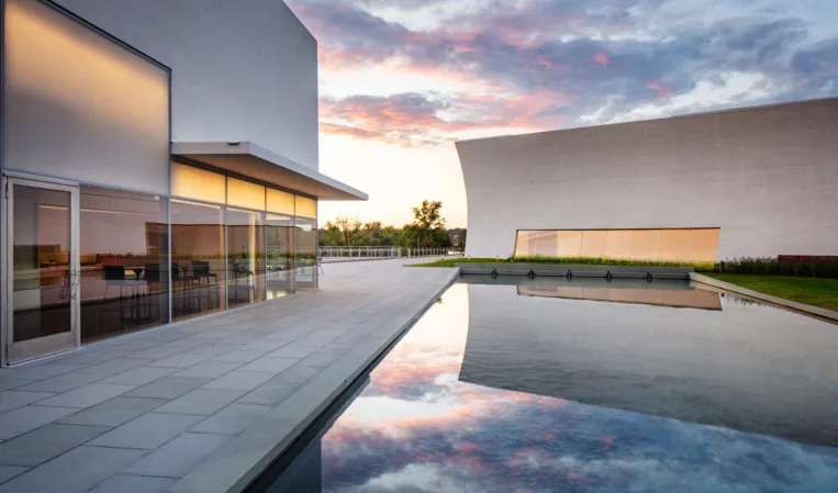 Large reflecting pool mirroring the evening sky between modern architectural buildings