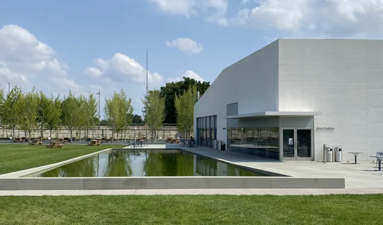 Rectangular reflecting pool surrounded by greenery beside a modern white building
