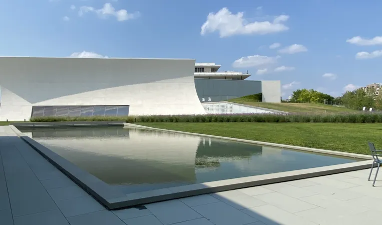 Rectangular reflecting pool surrounded by greenery beside a modern white building
