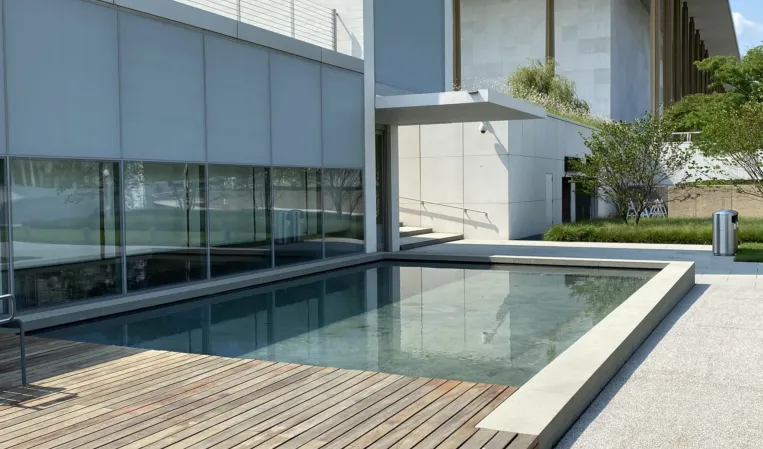 Rectangular reflecting pool with granite edges beside a modern building and wooden terrace