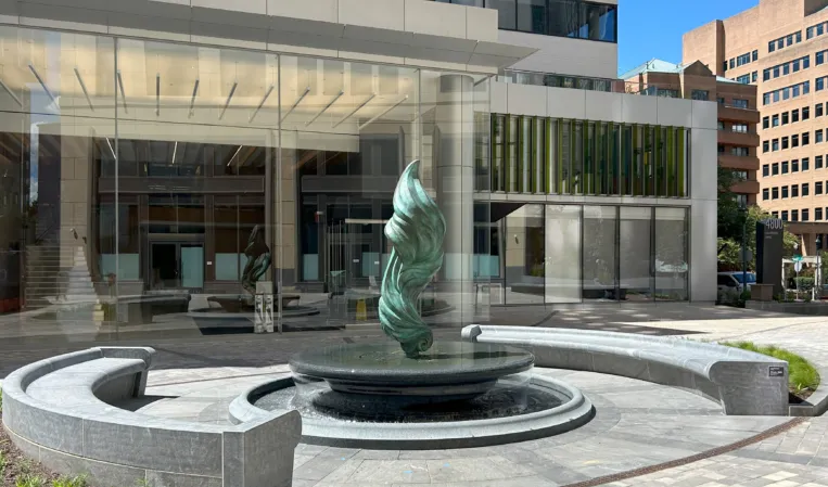 Bronze flame sculpture rising from a circular granite fountain in front of a modern office building