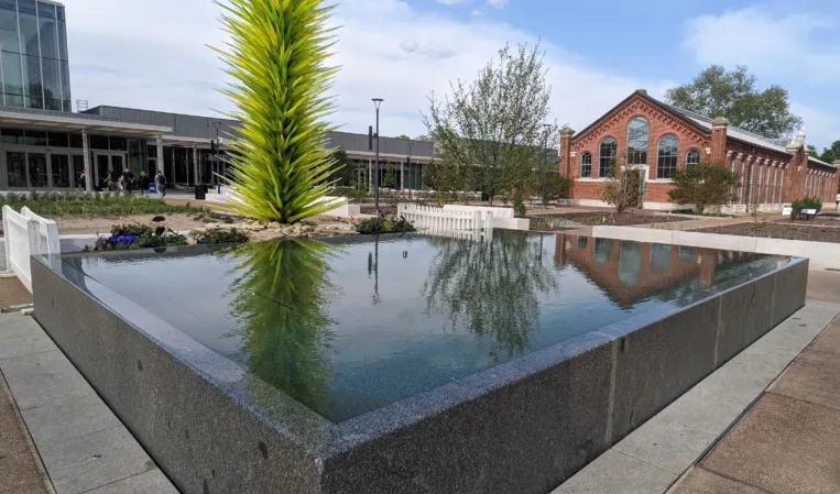 Rectangular granite reflecting pool with a tall green glass sculpture in an urban plaza