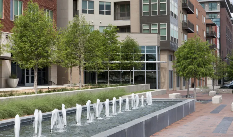 Linear granite fountain with water jets along a landscaped pedestrian walkway in a modern residential district