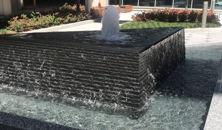 Granite fountain with a central water jet cascading over a textured stone wall into a lower basin