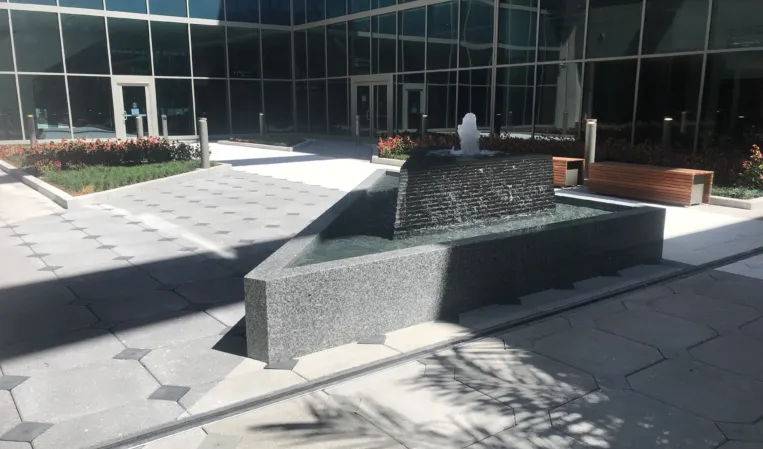 Granite fountain with a central water jet cascading over a textured stone wall into a lower basin
