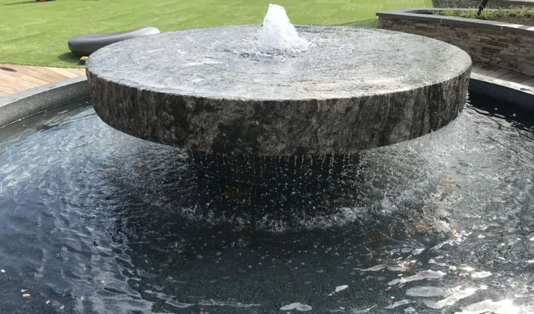 Circular granite fountain with a central water jet cascading over the edge into a lower basin