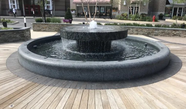 Circular granite fountain with a raised central basin and cascading water in an outdoor shopping plaza