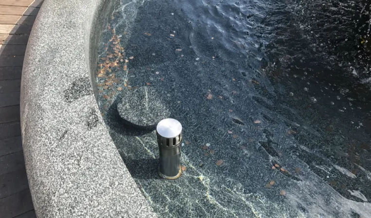 Close-up of a granite fountain basin with flowing water and an integrated stainless steel nozzle