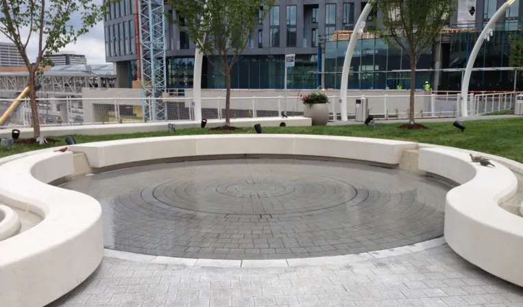 Circular paved fountain with concentric patterns and curved seating walls in a modern landscaped plaza