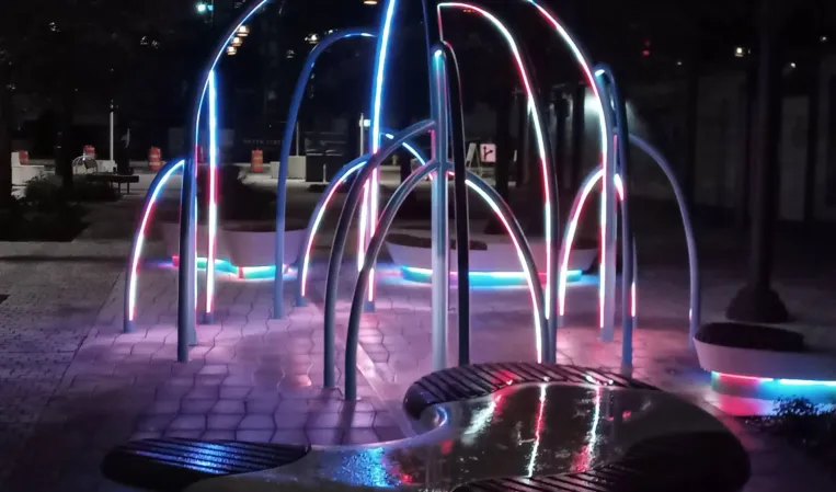 Illuminated interactive fountain with colorful curved arches and mist effects at night