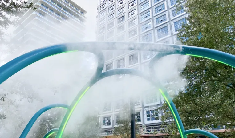 Curved fountain arches with mist and green lighting in front of modern office buildings