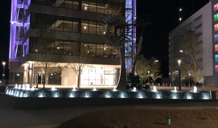 Illuminated fountain with rows of water jets outside a modern glass building at night