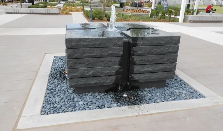 Fountain made of two stacked granite blocks with water jets flowing into a square pebble-filled basin