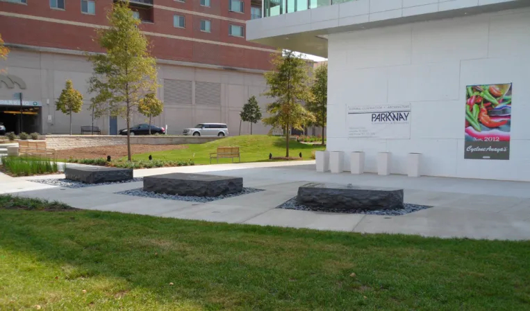 Three sculptural granite blocks surrounded by gravel in a landscaped urban plaza