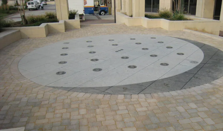 Circular paved plaza with embedded fountain jets in front of a modern building
