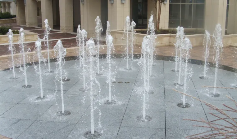 Circular interactive fountain with multiple water jets embedded in a paved plaza