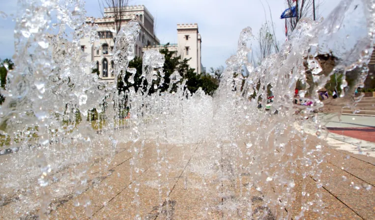 Close-up of interactive water jets spraying from a paved plaza with a historic building in the background