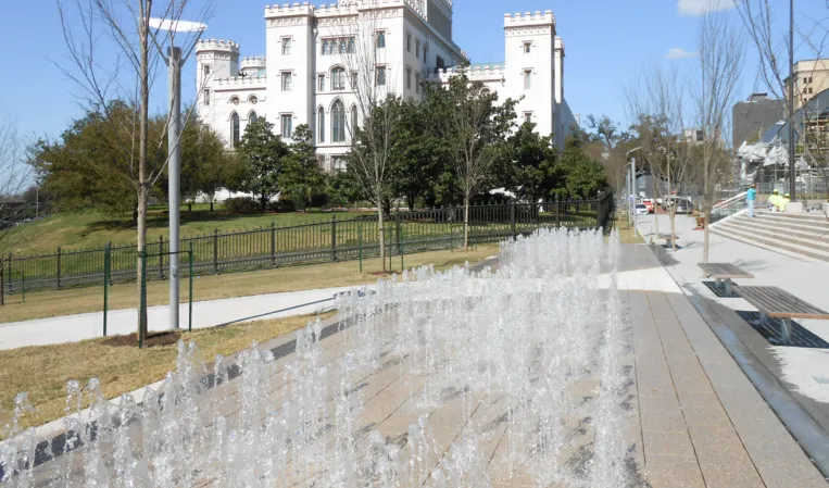 Rows of water jets in a paved fountain plaza with a historic castle-like building in the background