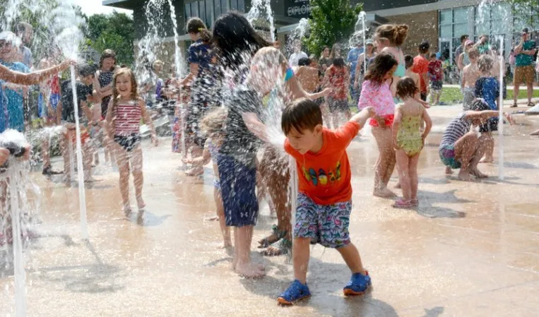 Children playing among interactive water jets in a splash fountain at an outdoor plaza
