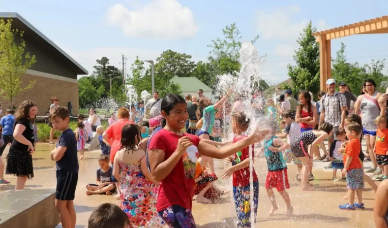 Children playing among interactive water jets in a splash fountain at an outdoor plaza