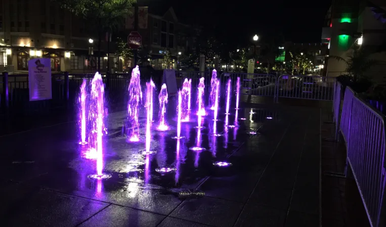 Interactive fountain with purple illuminated water jets in an urban plaza at night